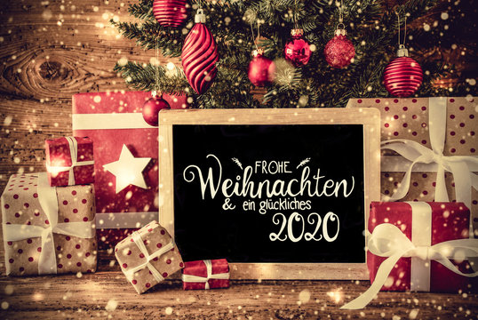 Blackboard With German Text Frohe Weihnachten Und Ein Glueckliches 2020 Means Merry Christmas And A Happy 2020. Christmas Tree With Decoration Like Ball, Snowflakes, Gifts And Presents