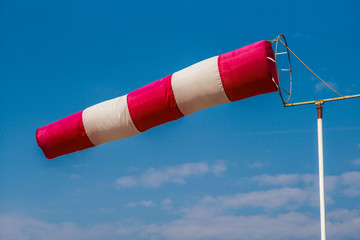 almost horizontally flying windsock (wind vane) with blue and light cloudy sky in the background.