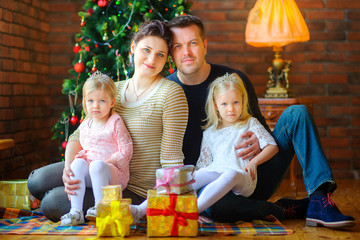 Portrait of a happy family celebrating Christmas at home, sitting on the floor near gifts