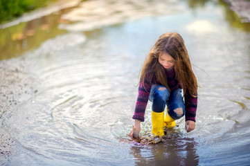 girl in yellow sopog plays in a puddle in a small boat, children's fun