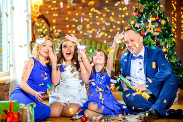 Portrait of a happy family celebrating Christmas at home, sitting on the floor near gifts, scattering sweets and having fun.