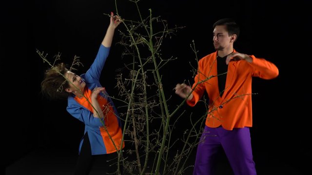 Crazy guy and girl in bright clothes make their way through the branches on a black background
