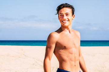 handsome teenager boy at the beach in swimwear looking at the back and smiling - attractive muscular young man on vacation having fun with the sea at the background © simona