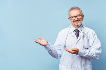 Cheerful mature doctor posing and smiling at camera, healthcare and medicine. Isolate on blue...