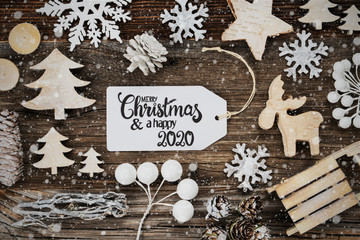 One White Label With English Text Merry Christmas And A Happy 2020. Frame Of Christmas Decoration Like Tree, Sled, Star And Fir Cone. Wooden Background With Snowflakes