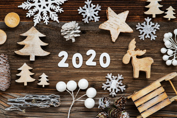 Obraz na płótnie Canvas White Letters Building The Word 2020. Wooden Christmas Decoration Like Tree, Sled And Star. Brown Wooden Background