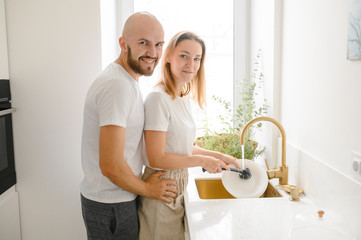 young happy couple is washing dishes while doing cleaning at home