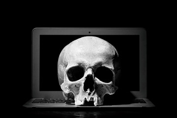 Cybercrime or hacking concept. Laptop in dark room under beam of light with a skull. Idea of virus...