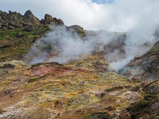 Colorful rhyolit red, orange and yellow fumarole at Reykjadalur valley with sharp rocks, grass meadow and geothermal steam. South Iceland near Hveragerdi city. Summer sunny day