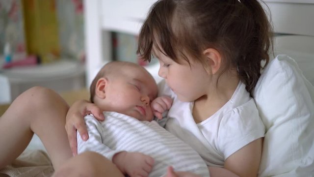 Big sister holding her newborn sister in her arms, taking care of little sister. Concept of love and child care. 