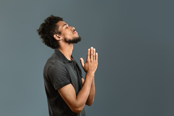 Portrait of African-American man praying against grey background