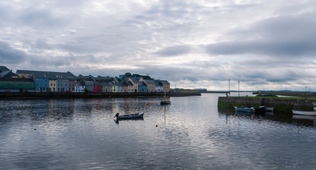 Fototapeta na wymiar Famous view of colorful Galway city houses and River Corrib with cloudy sky and boat on water. 