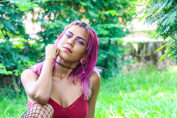 Relaxed young woman with pink hair posing in the park with many green plants in the background. Concept of feminine beauty.