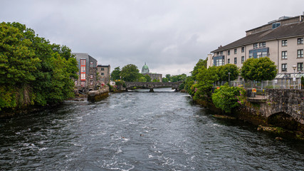 Fototapeta na wymiar View of the River Corrib flowing through Galway City Center with the old stone buildings and walkways through the quays and view of the Cathedral