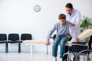 Fototapeta premium Young male doctor pediatrist and boy in wheel-chair