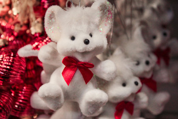 Christmas toy-white fluffy mouse, laughing, with a red bow hanging on a string on the background of blurred red Christmas balls, and the same cheerful mice