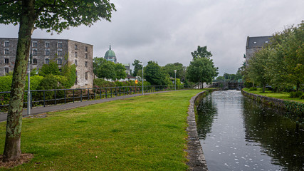 Fototapeta na wymiar City center Galway and the River Corrib with old buildings, bridges, fauna and cloudy sky. Taken in sumer.