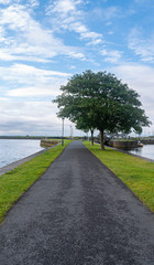 Footpath through park at Galway quay in the city, with trees, grass & sea on a sunny summer day.