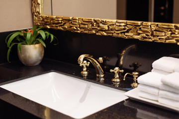 A stack of fresh white towels in the hotel's luxurious bathroom. A gold faucet, mirror and marble...