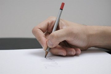male hand writing on white sheet of paper with a silver colored pencil
