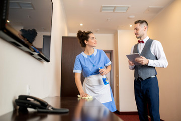 Pretty young room maid with detergent talking to porter in corridor of hotel