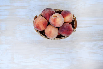 Peaches in a wicker basket on a light wooden table. Directly above