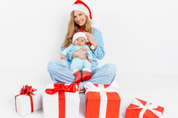 A young mother, on Christmas day gives a gift to a newborn child, a girl holds a baby in her arms with a Christmas gift