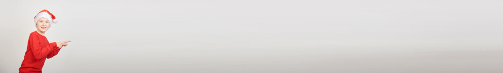Christmas banner of a cute little kid, teen boy wearing a Santa hat and red sweater isolated on a white background. Christmas holiday. The boy points his hand.