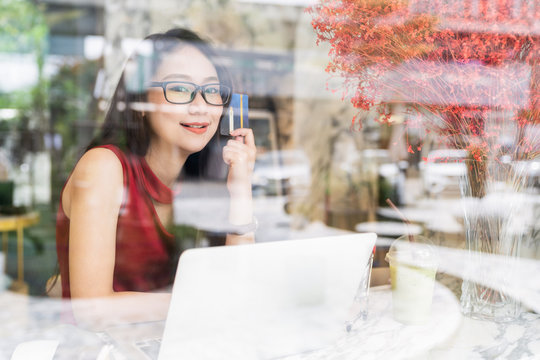 Online Banking and Payment concepts, Young asian woman sitting smiling holding credit card in hands while shopping online on laptop in coffee shop