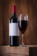 Bottle of red wine with label and wineglass on wooden background