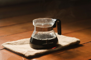Fresh coffee into a glass jug on cloth sack bag and wood floor in the morning.