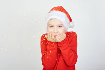 Christmas banner of a cute little kid blowing confetti, teen boy wearing a Santa hat and a red sweater, isolated on white background. Christmas holiday.