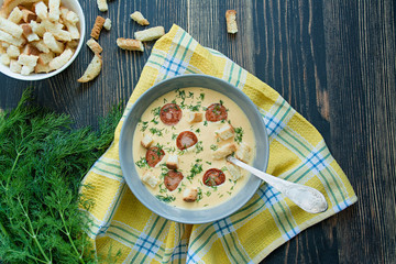 Cheese soup with grilled sausages and herbs. Cream soup served in a plate. Dark wooden background.