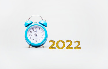 Time flies. Close-up photo of a turquoise clock, which shows five minutes to twelve, placed in the middle near the golden figures of 2022.