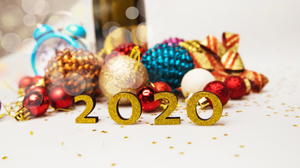 Christmas decorations. A composition of multicolored glittery Christmas decorations, a bottle of champagne, a sky blue alarm clock and golden numerals of 2020 in the front.