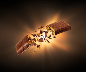 Chocolate bar with nougat is torn in the air with a flash of light in the dark