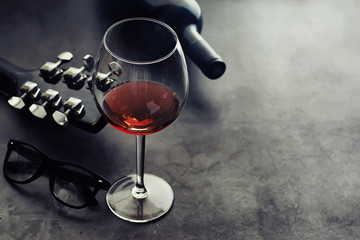 Guitar and high glass with red wine on a stone background.