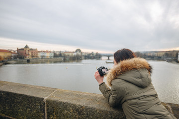 Fototapeta na wymiar Woman is taking pictures on the Charles bridge in Prague. Young beautiful girl tourist stands on the Charles Bridge in Prague in the Czech Republic and takes photos of beautiful city views