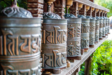 Tibetan prayer wheels, cylindrical rolls on a spindle made from metal and wood, selective focus. Translation: peace, happiness and health.