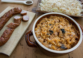 Bigos in stoneware dish and bigos ingredients: sausage, sauerkraut and cumin