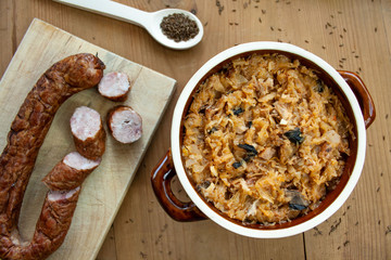 Bigos in stoneware dish and bigos ingredients: sausage, sauerkraut and cumin