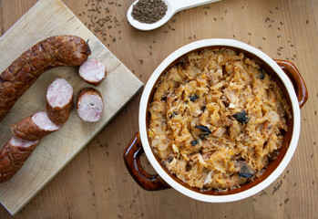 Bigos in stoneware dish and bigos ingredients: sausage, sauerkraut and cumin