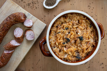 Bigos in stoneware dish and bigos ingredients: sausage, sauerkraut and cumin