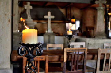 Old candle in candlestick holder in medieval pub. Christianity cross in background.