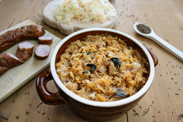 Bigos in stoneware dish and bigos ingredients: sausage, sauerkraut and cumin