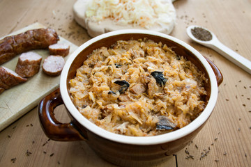 Bigos in stoneware dish and bigos ingredients: sausage, sauerkraut and cumin