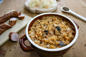 Bigos in stoneware dish and bigos ingredients: sausage, sauerkraut and cumin