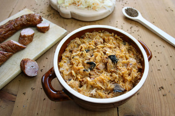 Bigos in stoneware dish and bigos ingredients: sausage, sauerkraut and cumin