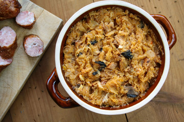 Bigos in stoneware dish and bigos ingredients: sausage, sauerkraut and cumin