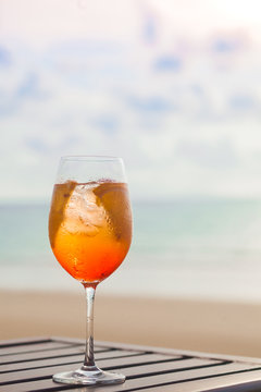 Delicious iced aperol spritz served on a small wooden table on a hot tropical beach in summer sunshine